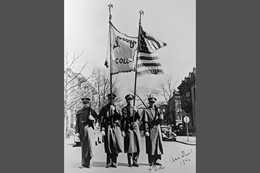 Four men in military dress holding two flags.